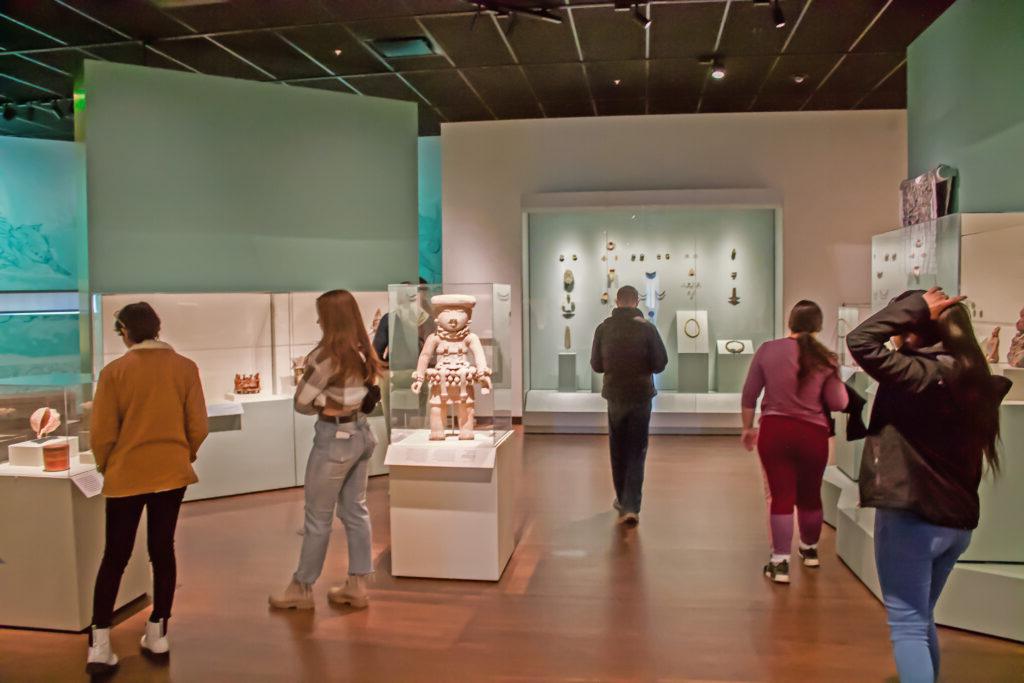 Students wander and observe ancient artifacts in a gallery.